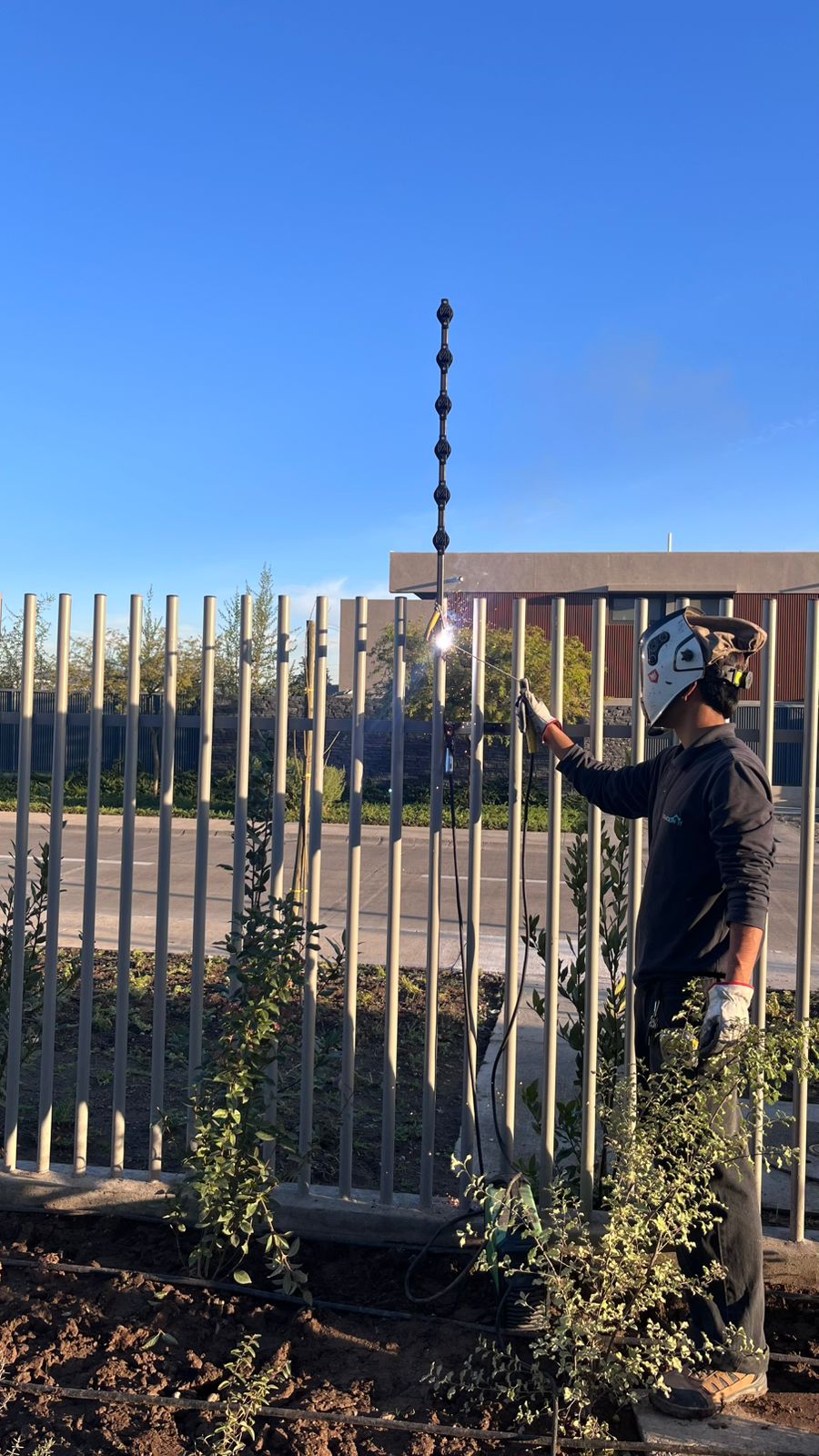 Técnico con máscara de soldar montando un soporte metálico para sensores de barrera perimetral en reja exterior